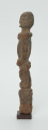 Drewniana figurka mężczyzny z twarzą zwróconą w prawo - Ujęcie z prawego boku; prawy profil drewnianej figurki człowieka. Prawa ręka płaskorzeźbiona wzdłuż tułowia. Noga przechodzi w długi cokolik.