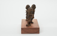 rzeźba - Ujęcie z prawej strony. Zestaw składa się z trzech małych, drewnianych figurek w pozycji stojącej przedstawiających postacie ludzkie wyobrażające przodków. Rzeźbom nie zaznaczono rysów twarzy, na szyi ozdobiono je żelaznym pierścieniem z podwójnym żelaznym wisiorkiem o trapezowatym kształcie.