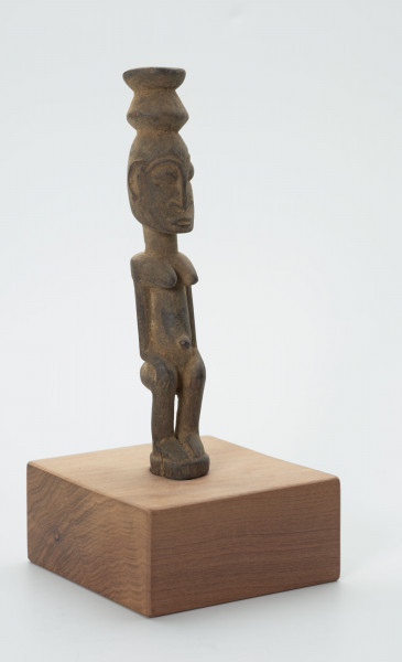 rzeźba - Ujęcie ze skosu z lewej; Figura - postać kobiety. Kobieta w pozycji siedzącej z naczyniem na głowie. Ręce spoczywają na kolanach.