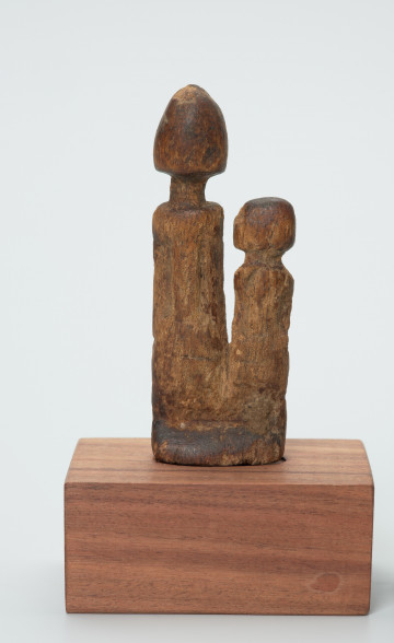 rzeźba - Ujęcie z przodu. Drewniane, rzeźbione dwie postaci ludzkie, różnej wysokości umieszczone na jednej podstawie. Bardzo schematyczne, z walcowatego tułowia wyodrębniona jedynie głowa na długiej szyi.