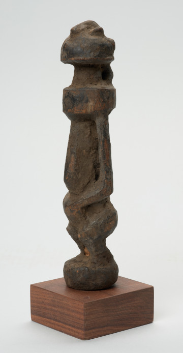 rzeźba - Ujęcie przodu skosem w lewą stronę. Rzeźba w drewnie w formie uproszczonej. Przedstawia postać męską o lekko zarysowanej głowie, szczupłym, długim tułowiu, krótkie nogi ugięte, ręce oparte na kolanach.