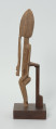 drewniana, rzeźbiona figura - Ujęcie lewego boku. Drewniana, rzeźbiona figura smukłej postaci znajdującej się w pozycji siedzącej. Długa broda ciągnąca się aż do kolan. Prawa dłoń spoczywa na kolanie, lewa trzyma brodę.