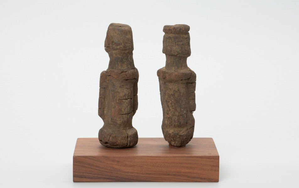 rzeźba - Ujęcie z tyłu; Zestaw składa się z dwóch małych, drewnianych figurek przedstawiających postacie ludzkie w pozycji stojącej. Rzeźby o uproszczonej formie i masywnej budowie ciała.