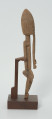 drewniana, rzeźbiona figura - Ujęcie prawego boku. Drewniana, rzeźbiona figura smukłej postaci znajdującej się w pozycji siedzącej. Długa broda ciągnąca się aż do kolan. Prawa dłoń spoczywa na kolanie, lewa trzyma brodę.