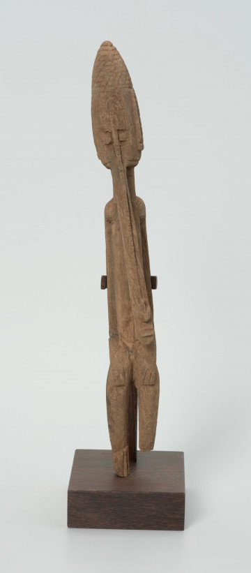 drewniana, rzeźbiona figura - Ujęcie z przodu. Drewniana, rzeźbiona figura smukłej postaci znajdującej się w pozycji siedzącej. Długa broda ciągnąca się aż do kolan. Prawa dłoń spoczywa na kolanie, lewa trzyma brodę.