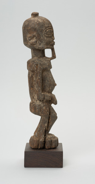 rzeźba - Ujęcie prawego boku. Figura przedstawiająca mężczyznę stojącego na nogach ugiętych w kolanach. Głowa duża, zaokrąglona, oczy duże, ze źrenicami, wyraźnie zaznaczona bródka.