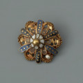 pontalik z sarkofagu księcia Franciszka I (1577-1620) - Ujęcie z przodu. Pontalik w kształcie kwiatowej rozetki z płatkami zdobionymi perełkami nawleczonymi na drut oraz emalią komórkową, inkrustowaną złotem. Płatki z perełkami otoczone są skręconym drutem. Środek kwiatka kopulasty, zbudowany z ośmiu białych płatków, zwieńczony złotą kulką. Na odwrocie centralnie przymocowane uszko z drutu.
