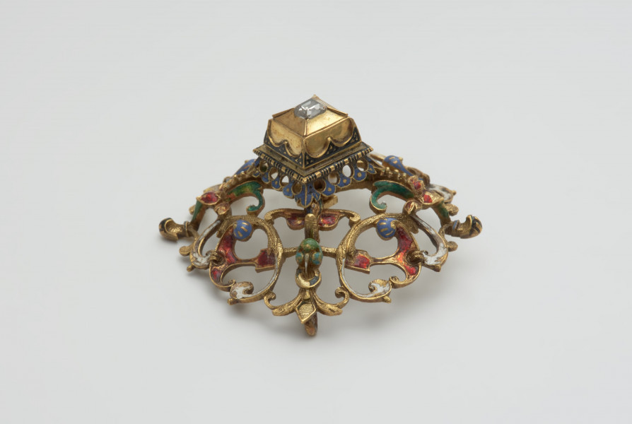 biżuteria, ozdoby - Ujęcie z boku z dołu. Ażurowy klejnot z kołpaka z diamentem, zdobiony barwną emalią.