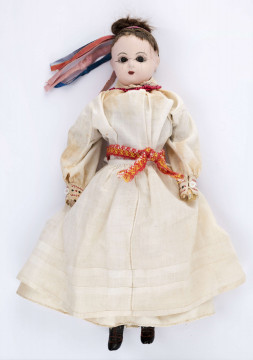 Ubiór kobiecy (model) na lalce. Składa się z bluzki haftowanej czarnymi i czerwonymi nićmi, fartucha, spódnicy i krajki. W warkocz wplecione różnokolorowe wstążki. Materiał fabryczny.