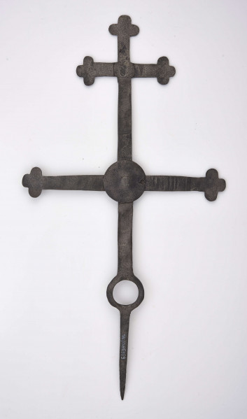Krzyż żelazny kowalskiej roboty wykonany ze sztabki szer. 2,3 cm i gr. 0,5 cm. Końcówka sztycy, jak i ramion, rozklepana i ukształtowana w formie krzyża o półkolistych ramionach. Górne ramię o szer. 15,7 cm znajduje się w odległości 7,5 cm od górnego zakończenia sztycy. Drugie ramię, dł. 32 cm, przymocowane jest do sztycy nitem, natomiast sposób łączenia zakrywają dwie tarcze o śred. 6,7 cm. W dolnej części sztycy znajduje się otwór o śred. 4 cm. Ostro zakończona sztyca wskazuje na zamocowanie krzyża na przydrożnej figurze lub kapliczce. 