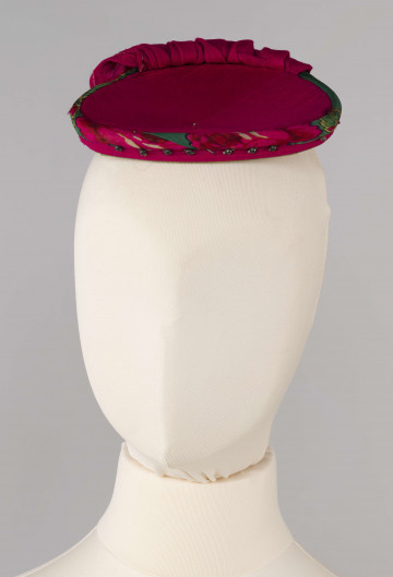 E/668/ML - Strój głowy mężatki wykonany z chustki fabrycznej koloru różowego w kwiatki, zawiązany na drewnianej obręczy. Przybrany paciorkami założonymi na szpilki.