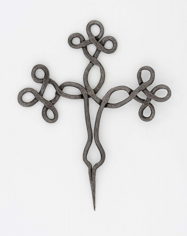 Krzyż żelazny stanowiący zwieńczenie drewnianego krzyża, kowalskiej roboty. Wykonany z pręta o śred. 0,7 cm. Ramiona i wierzchołek krzyża ozdobnie plecione. Szpikulec dł. 6,5 cm.
