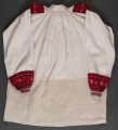 Koszula lniana o kroju przyramkowym, marszczonym. Ozdobiona na przyramkach i mankietach pereborami. Górna cześć koszuli wykonana z płótna lnianego bielonego, dolna – z szarego (dł. 30 cm). Kołnierzyk stójka (4 x 34 cm), zapinany na 3 guziki. Perebory czerwono-granatowe na przyramce (13 x 14,5 cm). Długość pereborów przy mankietach 12 cm. Mankiet (3 x 16 cm) z pętelkami do przeciągania tasiemki, w celu zawiązania.