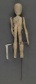 E/319/ML - Figurka z szopki, przedstawiająca śmierć, wykonana z drzewa, pomalowana białą farbą. Głowa o kształcie trójkątnym, wydłużonym. Oczy, nos i usta wydrążone i pomalowane srebrną farbą. Tułów krótki z zaznaczonymi plastycznie i zaznaczonymi srebrną i czarną farbą. Ręce ruchome w ramieniu, osadzone na drucie, w łokciu nieco zgięte z zaznaczonym plastycznie stawem łokciowym. Nogi proste, bez stóp, z silnie zgrubiałymi kolanami, z wyrzeźbionymi gwiazdkami pomalowanymi srebrną farbą. W rękach figurka trzyma kosę z drutu i cienkiej blaszki. Do ramienia przymocowany jest drut przechodzący z tyłu i założony za klamerkę wmontowaną w prawą nogę z tyłu. Drucik ten umożliwia poruszanie rękami figurki w czasie przedstawienia. W prawej nodze umocowany jest drut o haczykowatym zakończeniu.