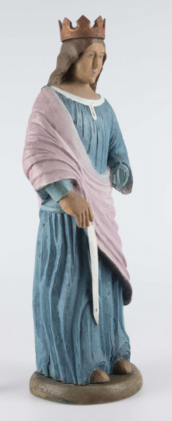 E/16790/ML - Rzeźba drewniana pełna polichromowana, przedstawiająca św. Katarzynę. Postać stojąca, ubrana w niebieską (wcześniej kolor ultramaryny) suknię, żłobioną  w fałdy, z białym wykończeniem przy szyi. Na wierzch, na prawe ramię, narzucony płaszcz/szal w kolorze jasnoróżowym. Prawa ręka opuszczona, trzyma miecz (obecnie samo ostrze koloru białego), lewa zgięta jest w łokciu – brak partii dłoni. Odsłonięte części ciała (stopy, dłonie, szyja, twarz) w kolorze jasnobrązowym; wcześniej prawdopodobnie beżowo-kremowe. Twarz owalna, brązowo-błękitne gałki oczne, usta różowe. Włosy brązowe, spływające fałdami do połowy pleców. Na głowie korona z 8 wierzchołkami, żłobiona, brązowa, uszlachetniona złotą farbą. 
Postać stoi na owalnej podstawie (22 x 19 cm), o wys. 3,5 cm, pomalowanej na brązowo (umbra), wcześniej – w szmaragdowej zieleni.