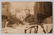 MPol/677/ML - Fotografia przedstawia dwóch mężczyzn siedzących przy stoliku w kawiarni, ubranych w mundury wojskowe. Z prawej strony Jerzy Pol z długimi wąsami i brodą. Obok niego kolega z ogoloną głową i krótko przystrzyżonymi wąsami. W tle widoczne wnętrze kawiarni ze stolikami nakrytymi białymi obrusami.