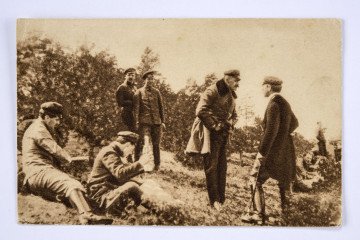 Pocztówka sepiowana - ćwiczenia Polskiej Organizacji Wojskowej w lesie pod Warszawą (zdjęcie grupowe w plenerze). Ujęcie w poziomie.
AWERS: grupa mężczyzn (ok. 10 osób) w mundurach austriackich lub ubraniach cywilnych; wśród nich komendant Józef Piłsudski; na pierwszym planie po lwej stronie dwóch siedzących na ziemi żołnierzy, po prawej Komendant Piłsudski (z dłońmi w kieszeniach spodni) rozmawiający z osobą w cywilnym ubraniu; na drugim planie pośrodku dwaj stojący żołnierze i po prawej stronie grupa siedzących osób; w tle drzewa.
REWERS: czarna linatura z miejscem na korespondencje; w l. g. rogu nadruk w postaci odznaki pamiątkowej 
