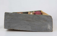 Płaskorzeźba w drewnie lipowym, polichromowana, przedstawiająca wnętrze kuchni, wykonana w jednym kawału drewna. Wnętrze kuchni zaznaczone z lewej strony występem szer. 6,7 cm i gł. 4,5 cm. U góry podkreślony „sufit” wys. 3 cm i gł. 5 cm. Na postumencie wys. 3,5 cm i gł. 4,5 cm. Z lewej strony zakomponowana postać kobiety (z profilu). Kobieta stoi lekko pochylona nad stołem, na którym wałkuje ciasto. Ubrana jest w długą czerwoną suknię w czarne kropki, z długim rękawem.  Na głowie ma zawiązaną, pod brodą, popielatą chustkę, spod której wystają czarne włosy. Twarz płaska, oczy lekko wypukłe, brwi czarne łukowate, nos długi prosty. 
Pod stołem stoi dzbanek, którego brzusiec ozdobiony jest czteropłatkowym kwiatem. Płatki w kolorze czerwony, środek zielony. Wylew podkreślony zielonym paskiem. Z prawej strony przy niskim brązowym stołku, po obu stronach stoją dzieci, które z jednej miski jedzą obiad. Z lewej strony stołka postać chłopca (wys. 12,5 cm) w szarych spodniach, sięgających za kolana i w zielonej koszuli wypuszczonej na spodnie. Twarz chłopca płaska, włosy czarne sięgające do ramion. W prawej ręce chłopiec trzyma łyżkę.  Z prawej – dziewczynka (wys. 13,6 cm), w długiej czerwonej sukience w żółto-czarne ciapki. Włosy czarne, sięgające ramion, twarz płaska. W prawej ręce trzyma łyżkę zanurzoną w misce, lewa opuszczona swobodnie. 
Na wys. 15,5 cm, z prawej strony, okno z kwiatami na parapecie i zasłonkami po bokach, do połowy okna. Wym. okna: wys. 14,5 cm, szer. 11,6 cm.