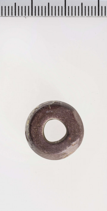 wykonany z łupka owruckiego; dwustożkowy, łagodnie profilowany; przy otworze płasko ścięty; otwór średniej wielkości, cylindryczny