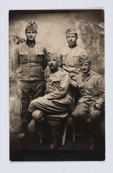 MPol/678/ML - Fotografia przedstawia czterch mężczyzn: dwóch siedzących i dwóch stojących za nimi. Wszyscy ubrani są w wojskowe mundury. Tło stanowi sztuczna sceneria imitująca roślinność.