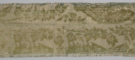 Pas tkaniny z motywami roślinnymi w kolorze żółto-zielonym. Na górze pas odbarwiony na niebiesko. Widoczny poziomy szew oraz trzy pionowe szwy sięgające od dołu do poziomego szwu. bryt Wil.Wn.132/1 - fragment, awers; ściana północna