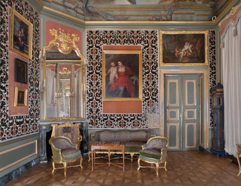 strona północna po prawej drzwi zielone ze złotymi listwami, po lewej kominek z lustrem w górnej części, ściany obite welurową tkaniną, wiszą obrazy, na pierwszym planie kanapa stolik i dwa fotele.