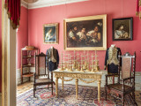 ściana wschodnia, różowa ściana z trzema obrazami, na pierwszym planie złoty stół ze złotymi paterami, po bokach 2 krzesła, na podłodze dywan.