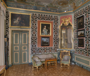 strona południowa po lewej drzwi zielone ze złotymi listwami, po prawej kominek z lustrem w górnej części, ściany obite welurową tkaniną, wiszą obrazy, na pierwszym planie kanapa stolik i dwa fotele.