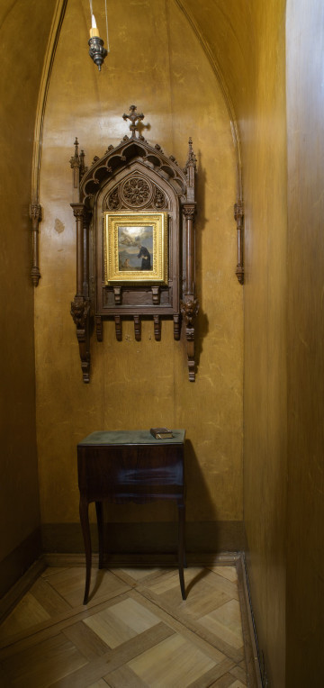 ściana zachodnia malowana we wzór przypominający drewno w centrum ołtarzyk na ścianie oraz niewielki stoliczek.