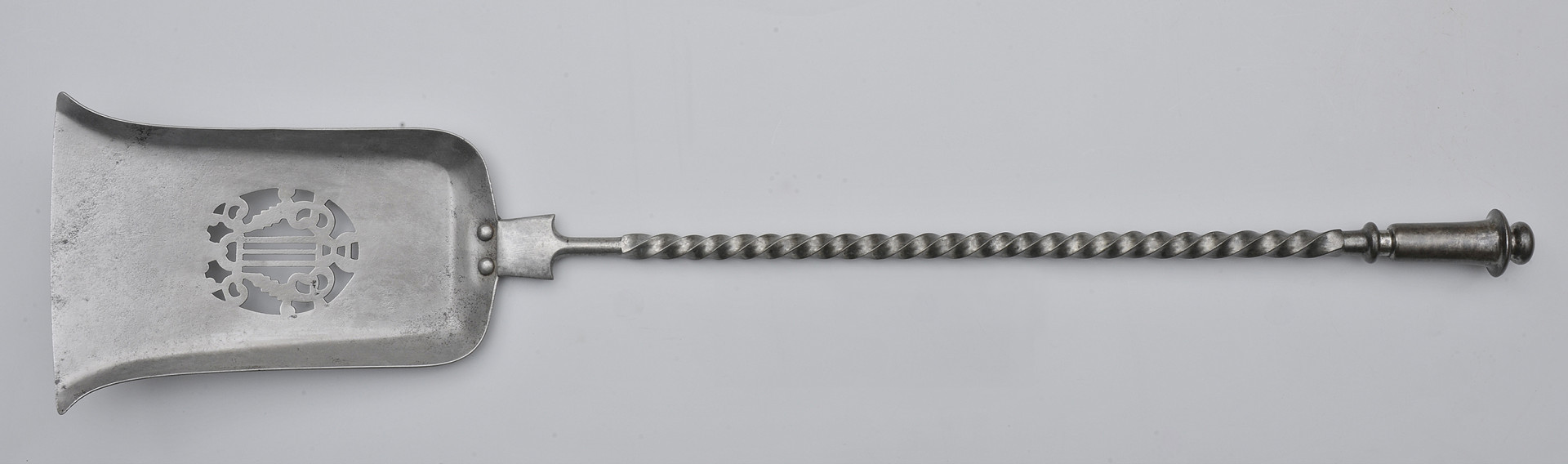 awers. Szufelka w orientacji poziomej, skierowana rączką w prawo. Czerpak wąski, lekko rozszerzony przy krawędzi, z ażurowym motywem liry pośrodku. Trzpień jest gęsto spiralnie skręcony. Rączka jest gładka, dzwonowato rozszerzająca się ku końcowi.