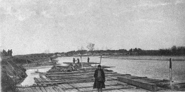 Fotografia czarno-biała przedstawia grupę mężczyzn pracujących przy spławie drewna.
