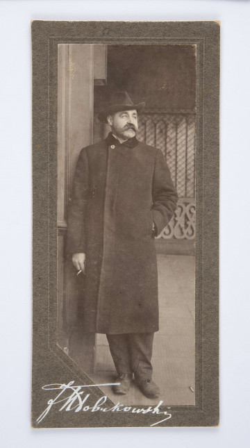Rafał Radziwiłłowicz, brat Oktawii Żeromskiej ubrany w płaszcz i kapelusz. Postać z zarostem, w dłoni trzyma papierosa.