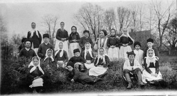 Fotografia czarno-biała plenerowa przedstawia grupę dzieci z opiekunką.