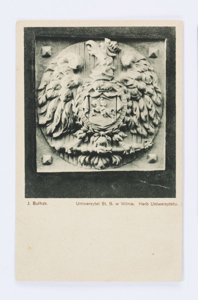 Pocztówka wykonana w sepii, przedstawiająca herb Uniwesytetu Stefana Batorego w Wilnie - płaskorzeźba z wizerunkiem orła w koronie, z wysoko uniesioną głową, skierowaną w lewą stronę; na piersi znak litewskiej pogoni. Na każdym z rofów kamienny ćwiek o ozdobnej główce.