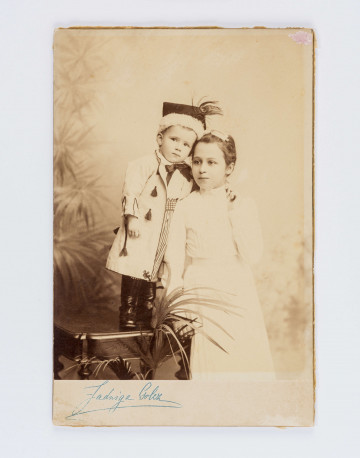 Chłopczyk około 4 lat w krakowskiej czapce z piórami i sukmanie stoi na stołku, obok dziewczynka w białej sukience.