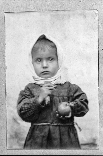 Fotografia czarno-biała przedstawia dziecko trzymające w lewej ręce jabłko.