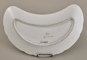 Talerzyk przystawkowy, w kształcie półksiężyca, z wyzębionym brzegiem, biały, z koroną hrabiowską. Tył