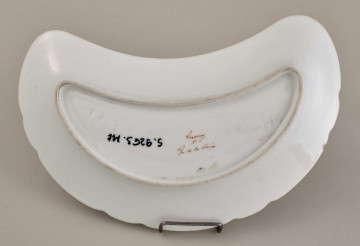 Talerzyk przystawkowy, w krztałcie półksiężyca, z wyzębionym brzegiem, biały,z koroną hrabiowską. Tył