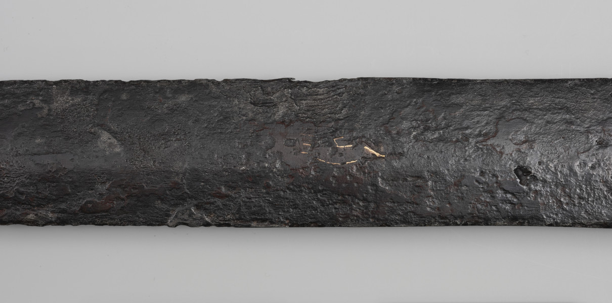 Miecz dwuręczny typu XVIII (Oakeshott) - detal; Ujęcie fragmentu głowni. Widoczne pozostałości po rytych znakach wypełnione żółtym metalem.