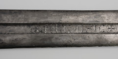 Miecz jednoręczny typu XII (Oakeshott) - detal; Na zbroczu i na końcu krzyż wpisany w okrąg, pomiędzy krzyżami napisy ryte i wypełnione srebrnym metalem. Płaszczyzna NRCDISIC;