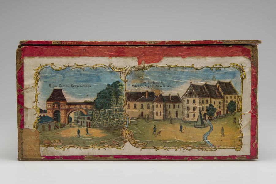 Lewy bok skrzynki z dwoma podpisanymi widokami, po lewej: „Ruiny Zamku Krzyżackiego”, po prawej: „Domu Urodzenia Mikołaja Kopernika w Toruniu”.
