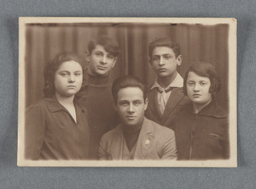 Wykonane w atelier zdjęcie pięciu młodych osób w dwóch rzędach na tle ciemnej kotary, po lewej kobieta sportretowana m.in. na zdjęciu nr 1.9.Fotografia z prostymi krawędziami, jasny niewielki margines przy każdej.