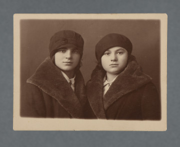 Fotografia dwóch kobiet: po lewej Mania Żelazna, po prawej koleżanka widoczna również na innym zdjęciu (z datą w dedykacji 6.01.1930, nr MPOLIN-A48.1.10); popiersie, obu w ciemnych płaszczach z kołnierzem, takich samych, białych koszulach z kołnierzykiem pod płaszczami, oraz w ciemnych nakryciach głowy: kobieta po lewej w kapeluszu typu hełm (z niewielkim daszkiem) i ozdobą na pasku przypominającą kwiat, kobieta po prawej w berecie. Twarze owalne, ujęte na wprost, patrzą w obiektyw. Krawędzie proste, z białym marginesem.