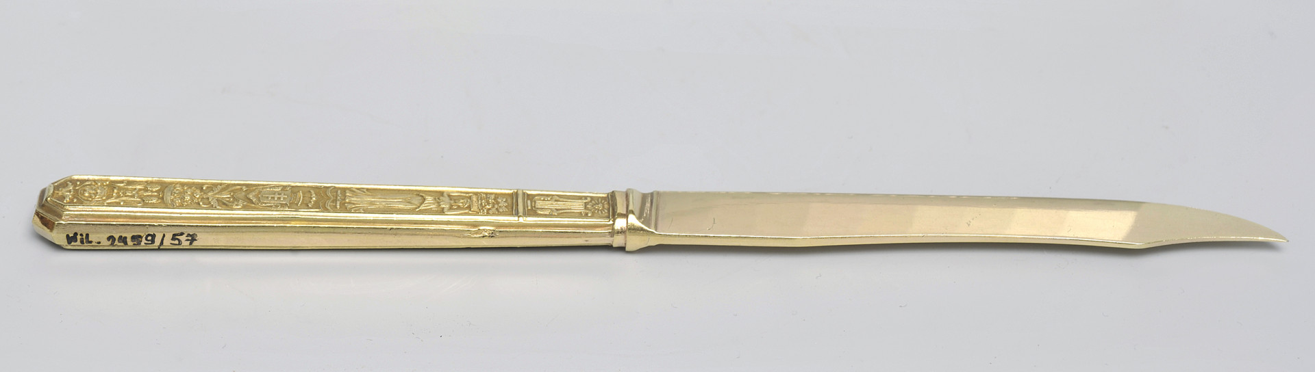 ujęcie 3/4 -&nbsp;strona z&nbsp;gładką głownią. Ujęcie z&nbsp;widocznym grzbietem. Czubek ostrza skierowany w&nbsp;prawą stronę. Na końcu górnej krawędzi trzonka numer inwentarzowy.