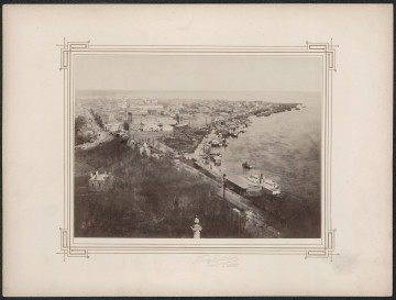 pośrodku białej karty zdjęcie z lotu ptaka na panoramę miasta. Dookoła fotografii drukowana ramka, zdobiona w narożnikach geometrycznym wzorem 