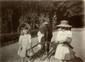 Na zdjęciu znajduje się dwie dziewczynki w kapeluszach trzymające kuca za uprząż. 