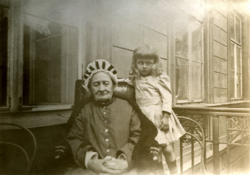 Fotografia prezentuje 3-4 letniego chłopca stojącego obok prababki.
