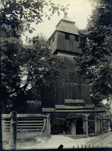 Na zdjęciu znajduje się drewniany kościół między drzewami.