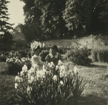 Na zdjęciu znajduje się dwie dziewczynki pośród kwiatów w ogrodzie.