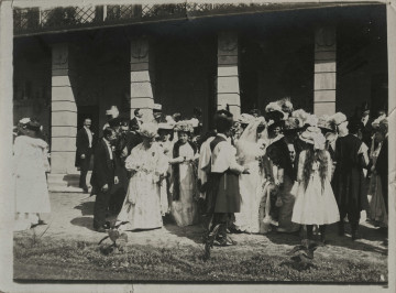Na zdjęciu znajduje się grupa osób odświętnie ubranych, zgromadzonych przed pałacem.